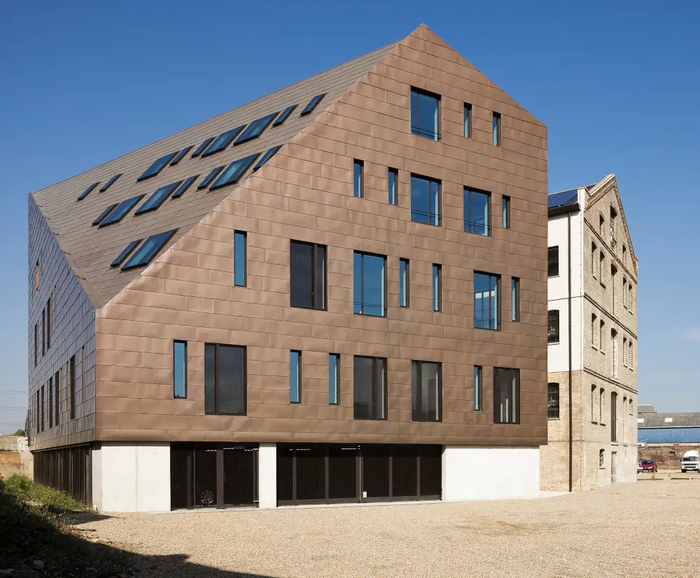 Modern architectural building with angular roof design and large windows, known as The Granary, set against a clear blue sky.
