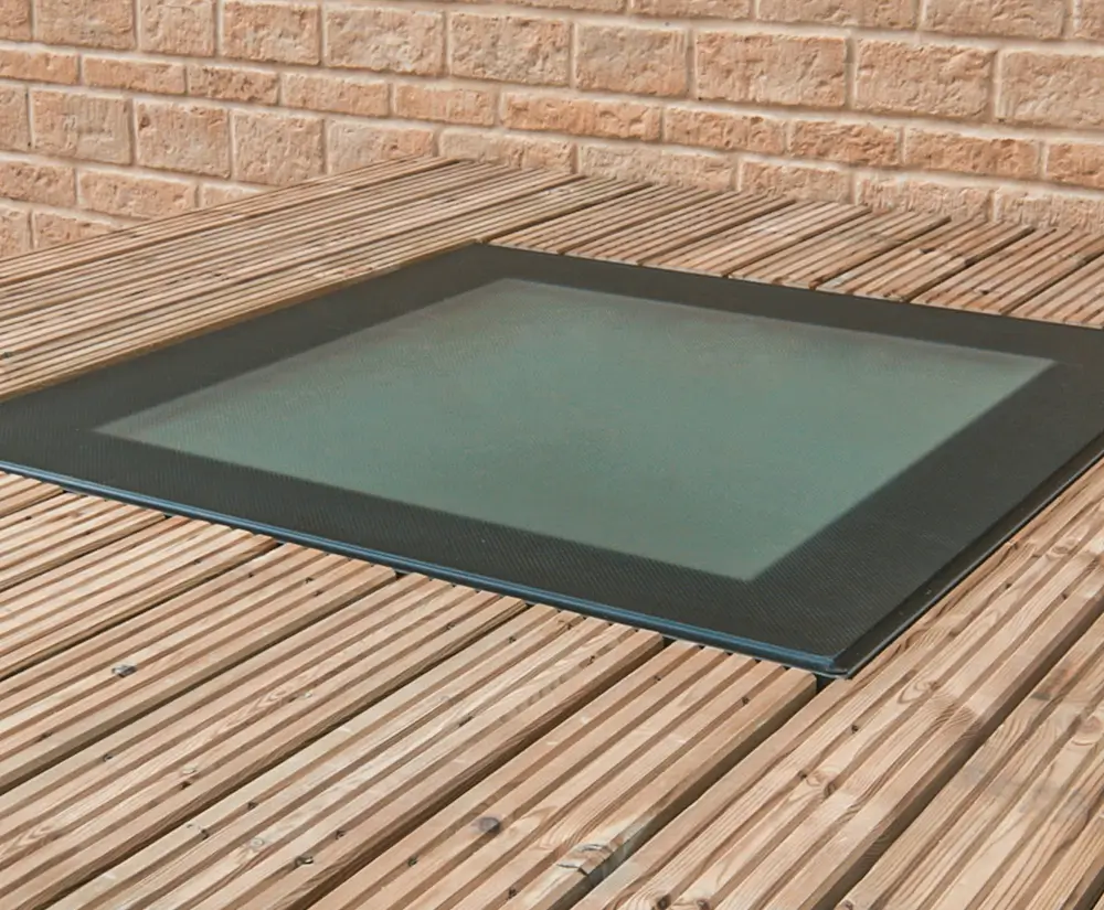 Modern flush rooflight installation on wooden decking with brick wall background.